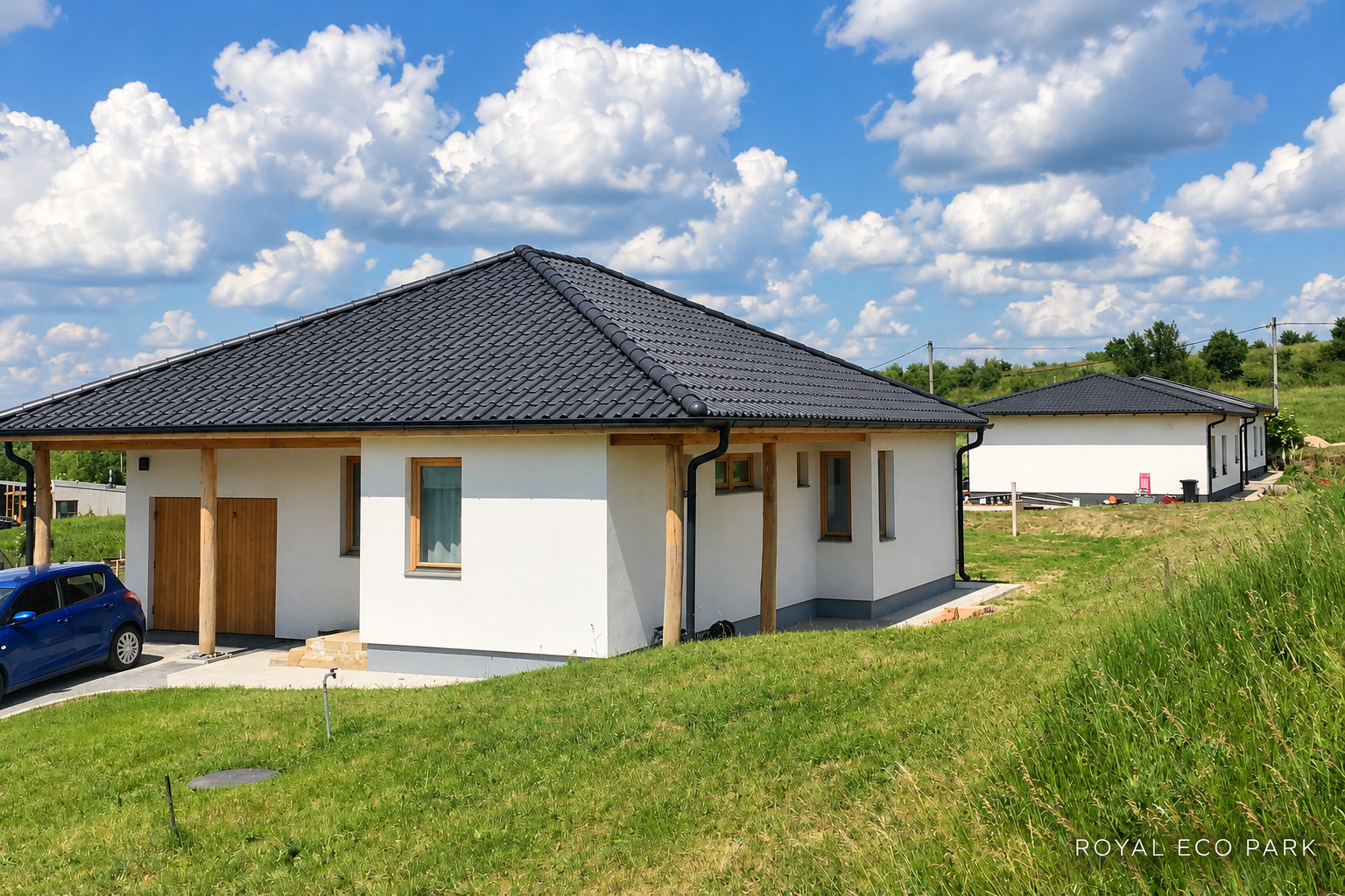 Füves domboldal fehér házakakkal, sötét tetőkkel és kék, felhős éggel